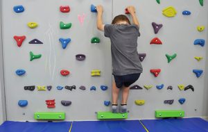 ćwiczenia na stopy płasko-koślawe na ściance wspinaczkowej. Dziecko stoi na ściance wspinaczkowej na palcach w półprzysiadzie