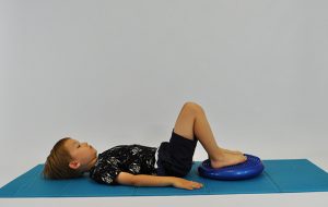 ćwiczenia na pośladki. Dziecko leży tyłem nogi ugięte na poduszce sensorycznej