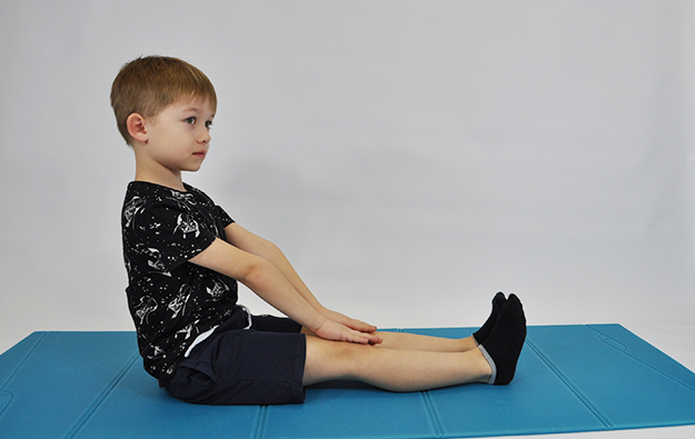 ćwiczenie rozciągające mięśnie kulszowo-goleniowe. Dziecko w siadzie prostym prostuje kolana